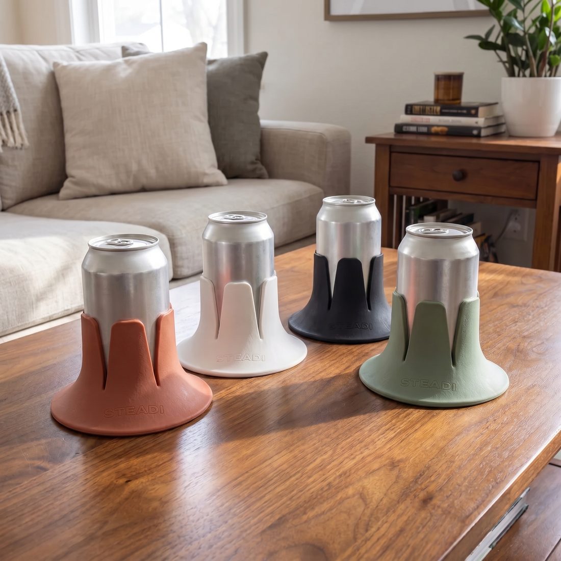 Four Steadis in terracotta, white, charcoal and sage, each holding a can, along a wooden table.